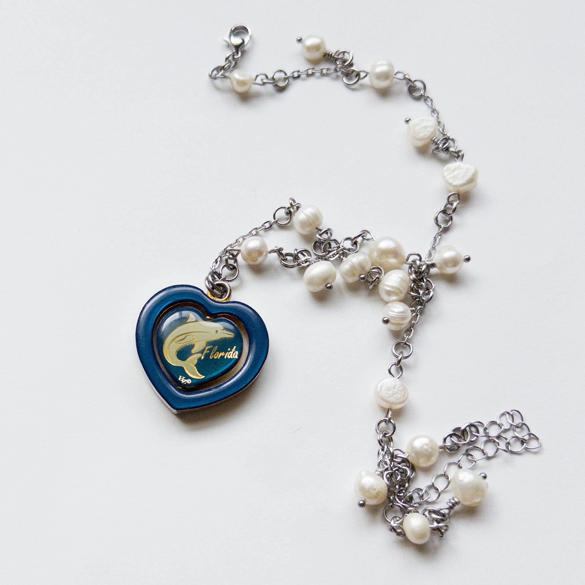 pearl necklace with a spinning heart pendant. the pendant has a white dolphin and text that said "florida".