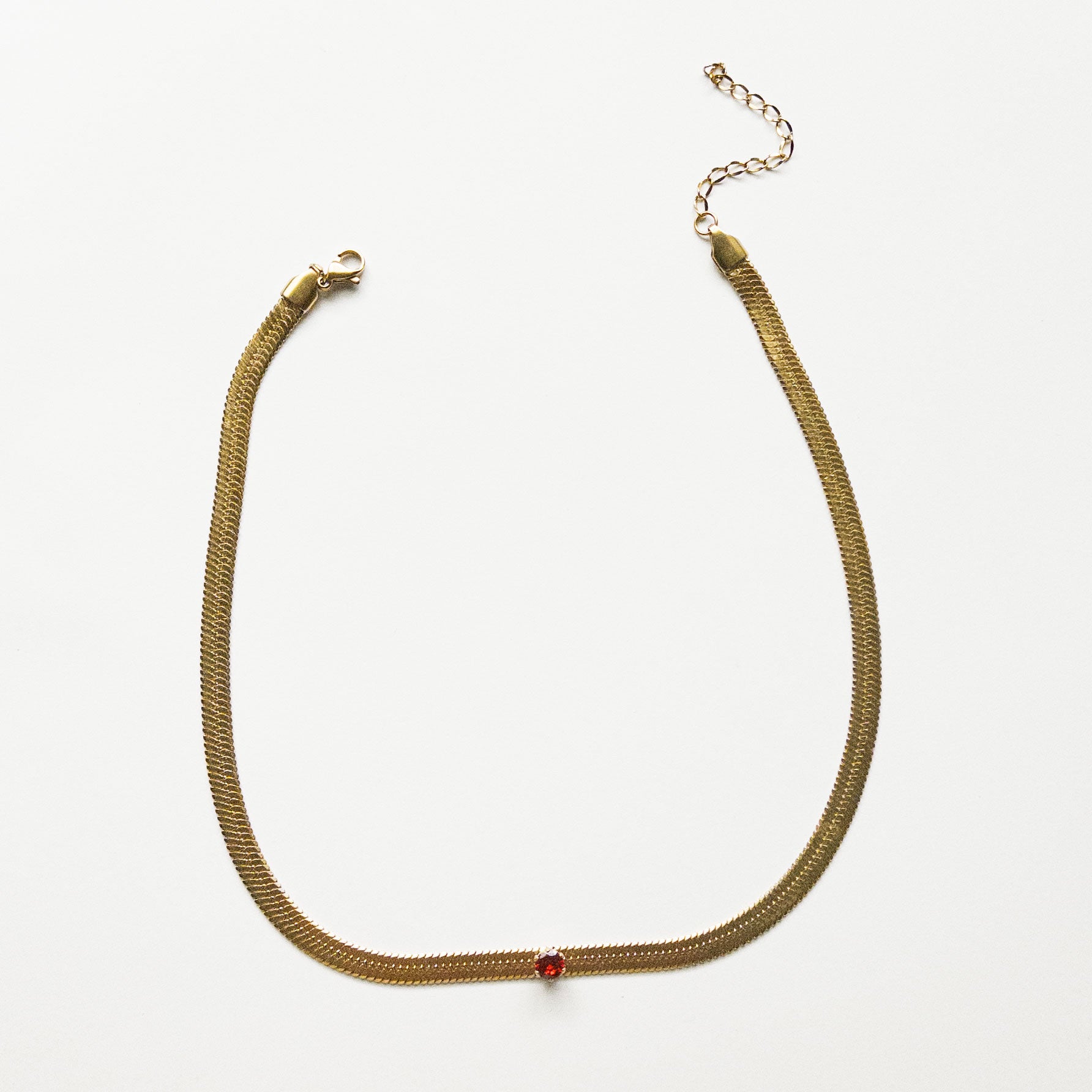 Stainless steel gold colored snake chain choker/necklace featuring a ruby red cubic zirconia gem in the center. Can be dress up or down. Perfect for layering and everyday wear. 