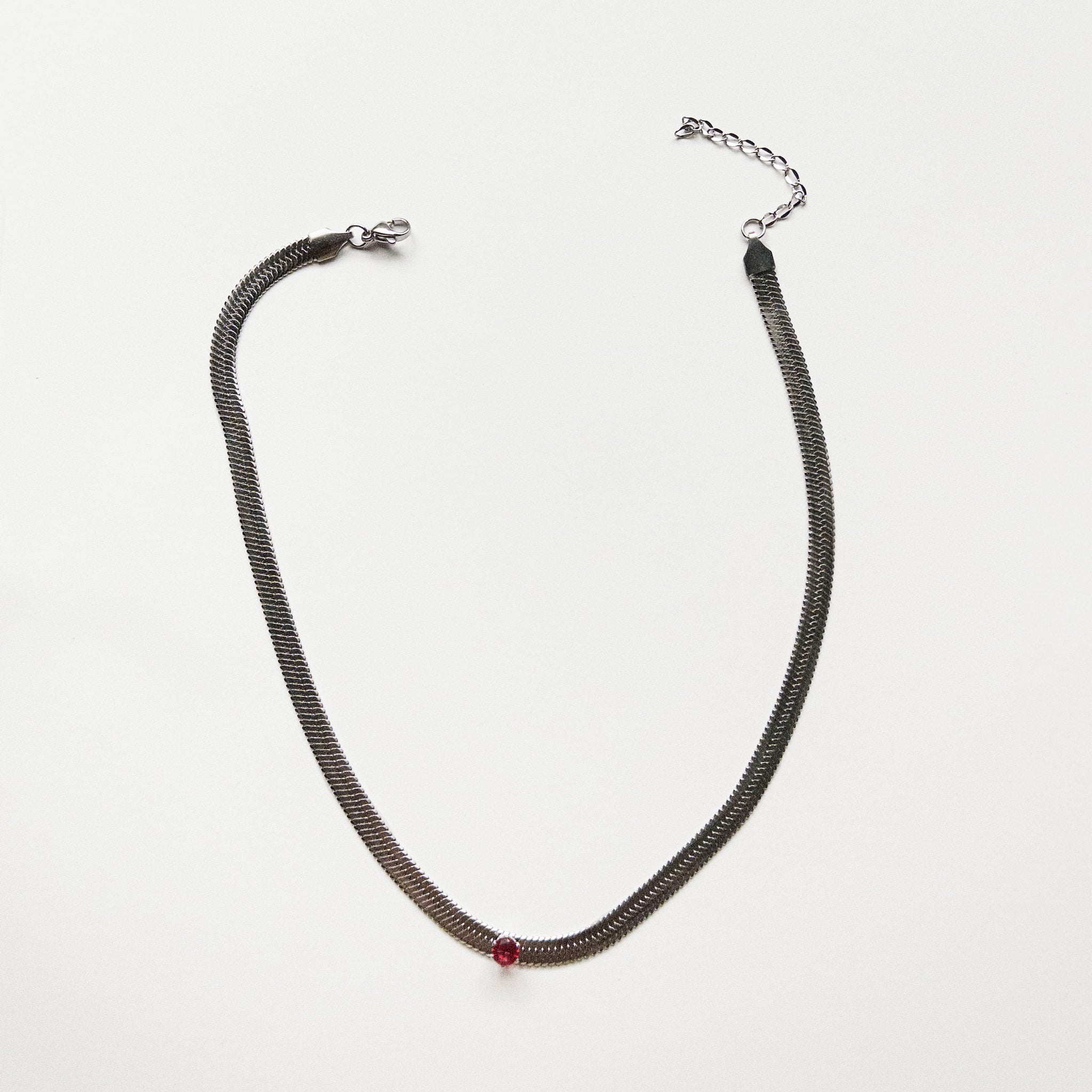 Stainless steel silver colored snake chain choker/necklace featuring a red ruby cubic zirconia gem in the center. Can be dress up or down. Perfect for layering and everyday wear. 